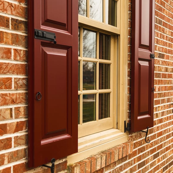 Dark red panel and louver shutters red brick and white siding house front left side first floor window cropped 2 wide social edit