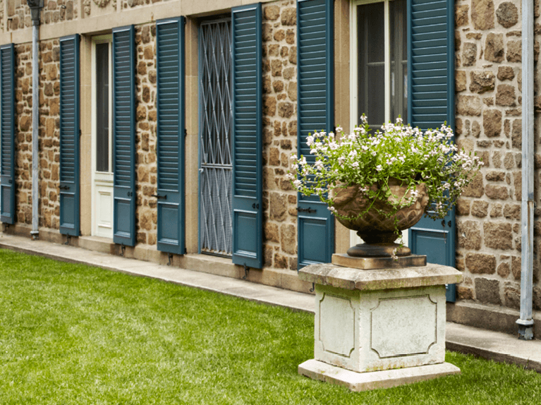 Timberlane blue combination panel and louver style shutters featured on a stone home exterior