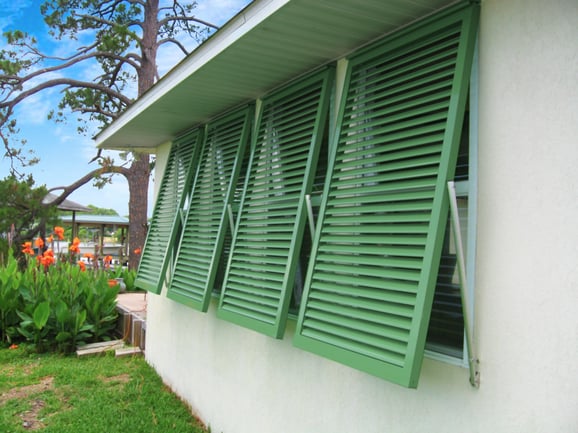 Green Resilience Bermuda Shutters on white stucco house angled