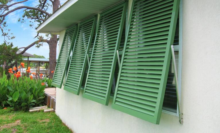 white coastal home with green hurricane rated bahama shutters and functional hardware