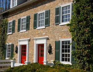 green operable louver and panel shutters on tan stone home