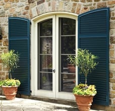 Blue fixed louver shutters with arch tops on tan stone home