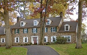 Stone colonial house with white panel shutters on the first floor and green louver shutters on the second floor