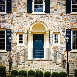 bLUE PANEL SHUTTERS ON ENTRANCE OF TAN STONE HOME