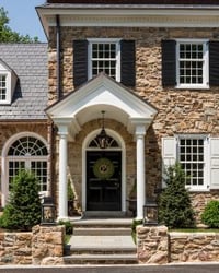 Black louver shutters and white panel shutters on tan stone home