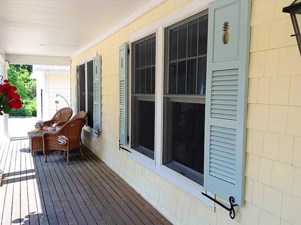 Light blue louver and panel combination shutters with pineapple cutout tan shakes house front porch angled