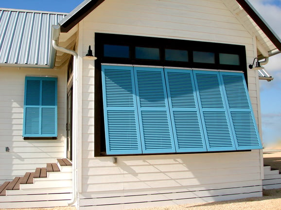 Teal blue bermuda shutters on white siding house side angled