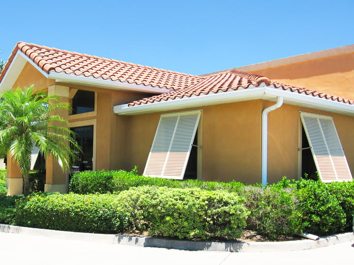 White Resilience Bermuda Shutters on yellow stucco house front angled