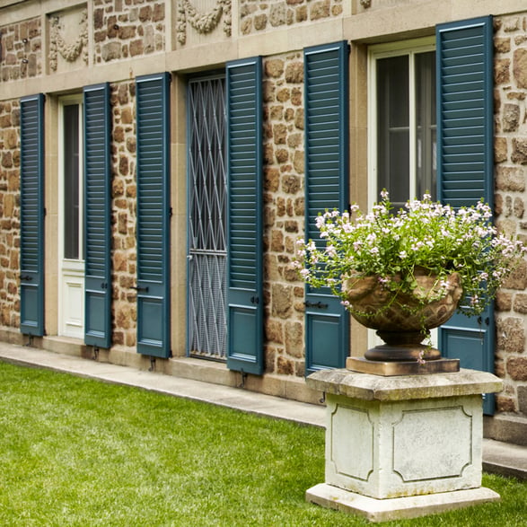 Blue louver and panel combination shutters tan stone home first floor angled social edit