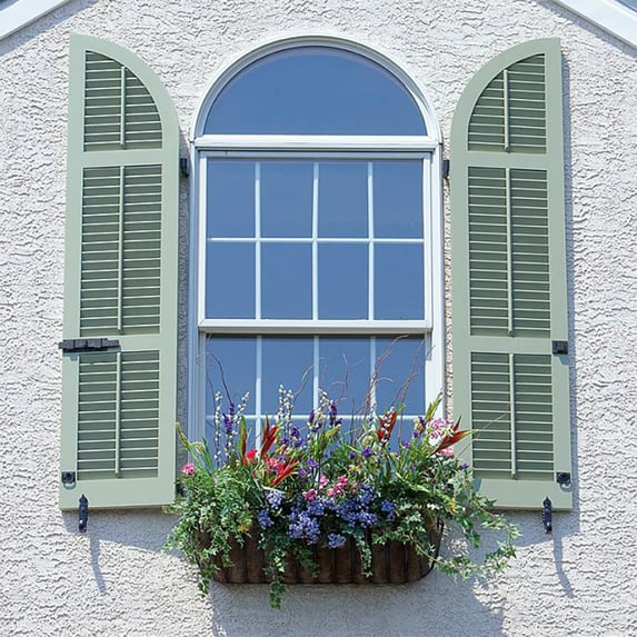 Pale green operable louver shutters with radius tops on gray stucco house single window top floor-social edit